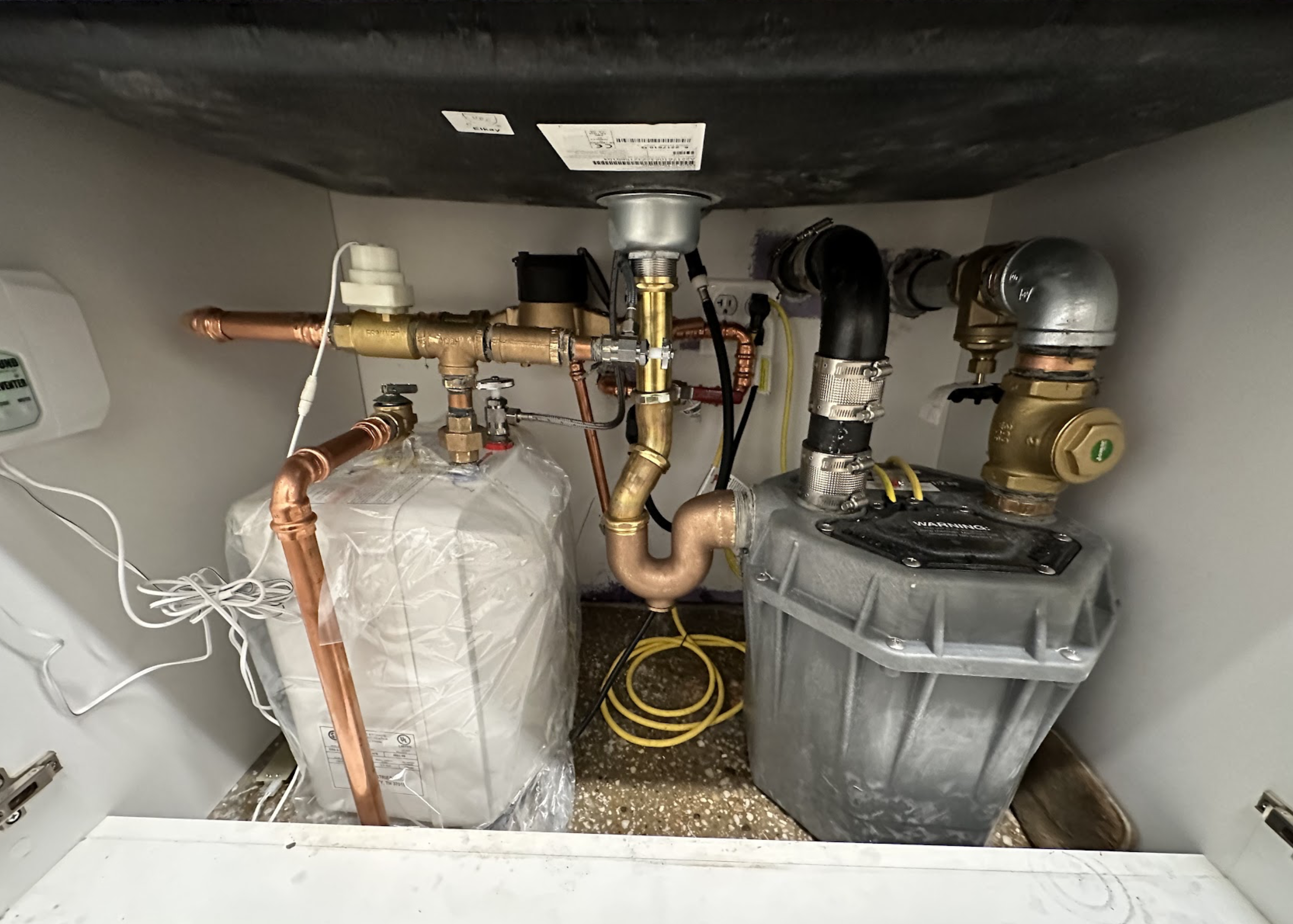 Under-sink water filtration system with white supply lines, brass ball valves, black drainage, and filter housing installed in a Forest Hills co-op kitchen
