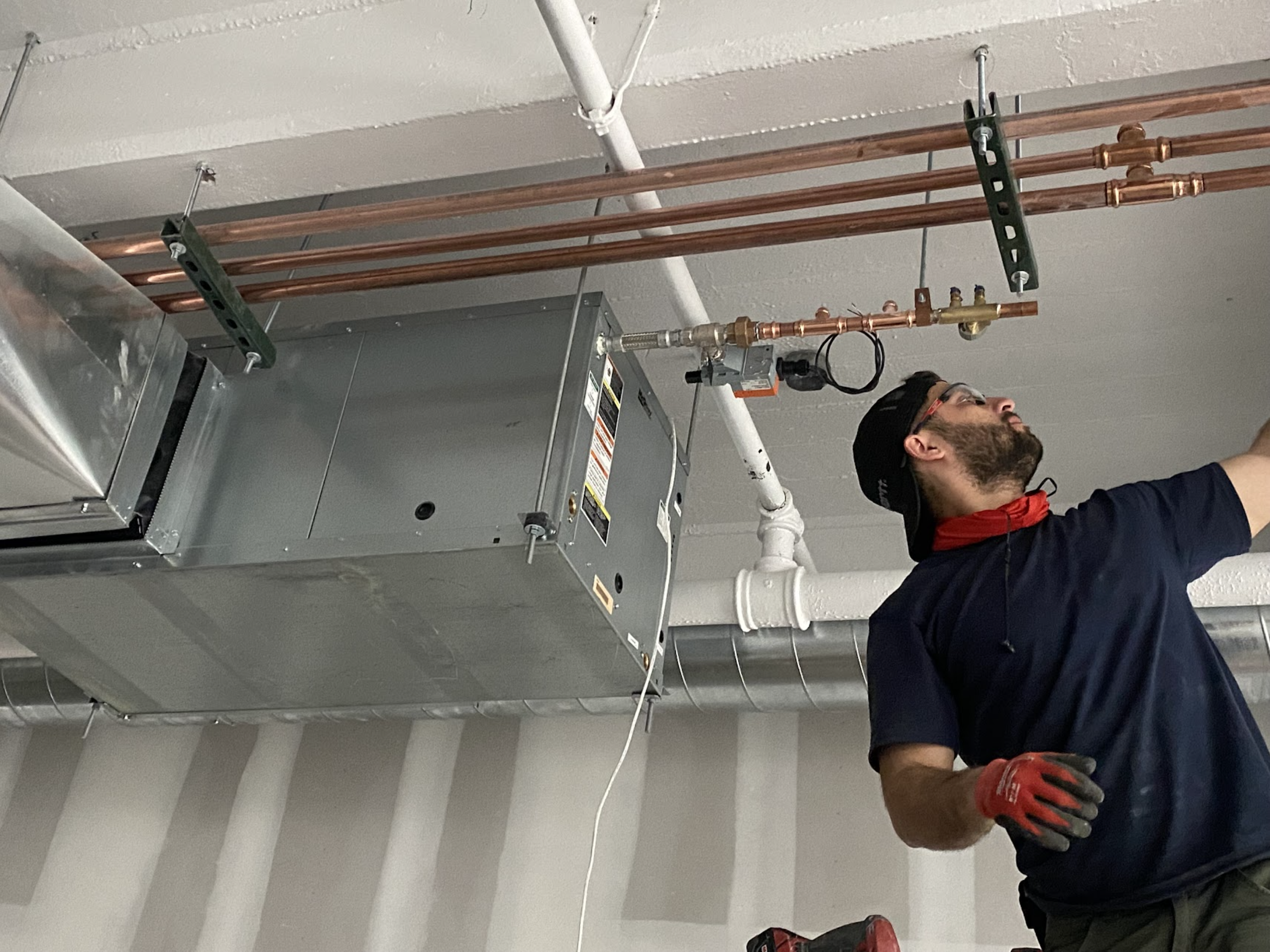 We Pipe LLC technician inspecting a ceiling-mounted fan coil unit with copper piping in Glendale, Queens