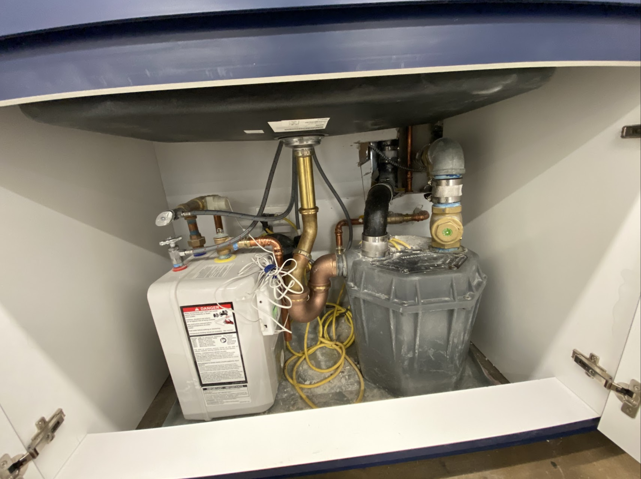 Compact point-of-use electric under-sink water heater with copper supply lines and brass fittings installed in a Long Island City condo bathroom vanity