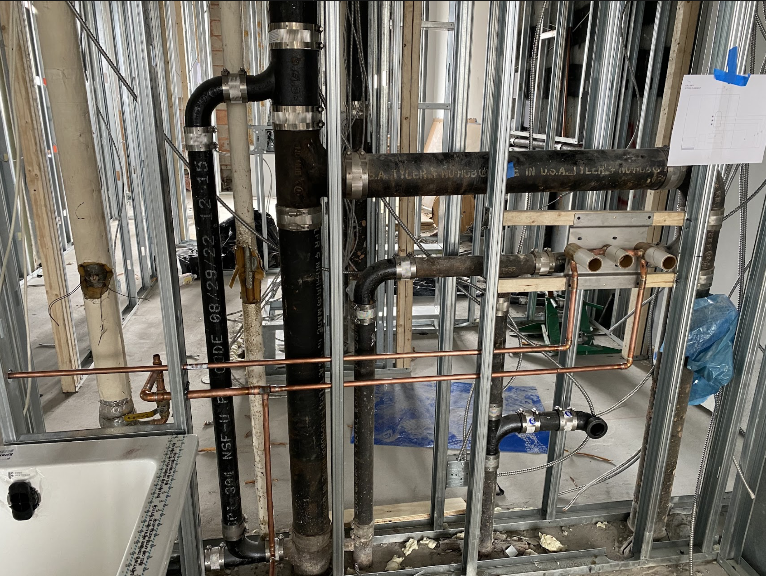 Concrete slab with drain rough-in opening showing black PVC piping and blue drain flange set for a floor drain installation in a Maspeth commercial conversion