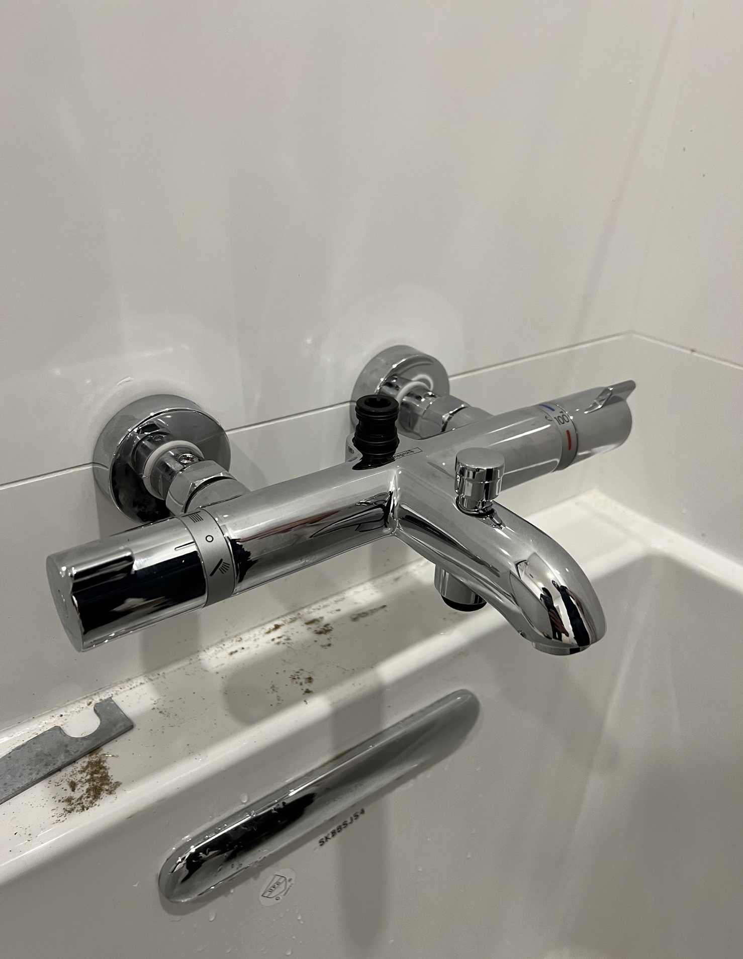 Chrome wall-mounted tub faucet and spout with shower valve trim installed on white tile in a Rego Park apartment bathroom renovation
