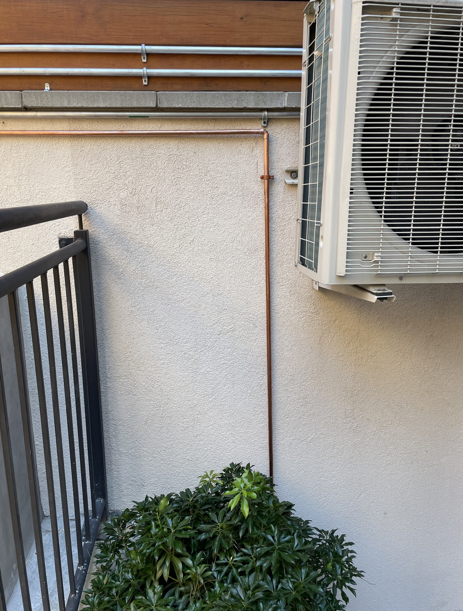 Copper refrigerant tubing and PVC condensate drain in white line-hide conduit on the exterior brick wall of a pre-war Ridgewood two-family for a ductless mini-split HVAC installation